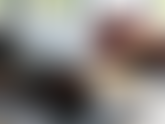 Two people in child’s pose on yoga mats indoors. One wears gray, the other maroon. A patterned blanket and cards nearby. Calm setting.