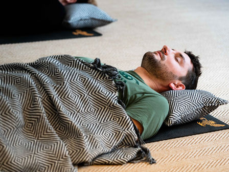A man lying on his back under a chevron blanket, practicing breathwork.