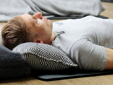 Person lying comfortably on a mat with a cushion under their head during a guided breathwork session.