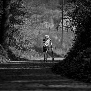 Wielrenner loopt naast zijn fiets tijdens een beklimming in de Brabantse Pijl Cyclo 2025, vastgelegd in zwart-wit.