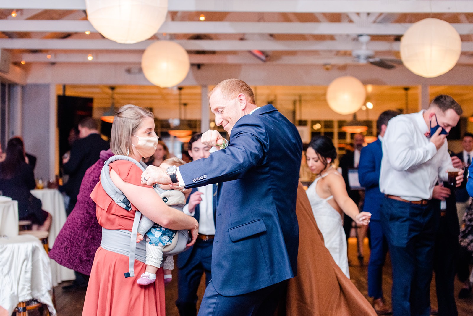 man and woman dance while holding a baby at a wedding
