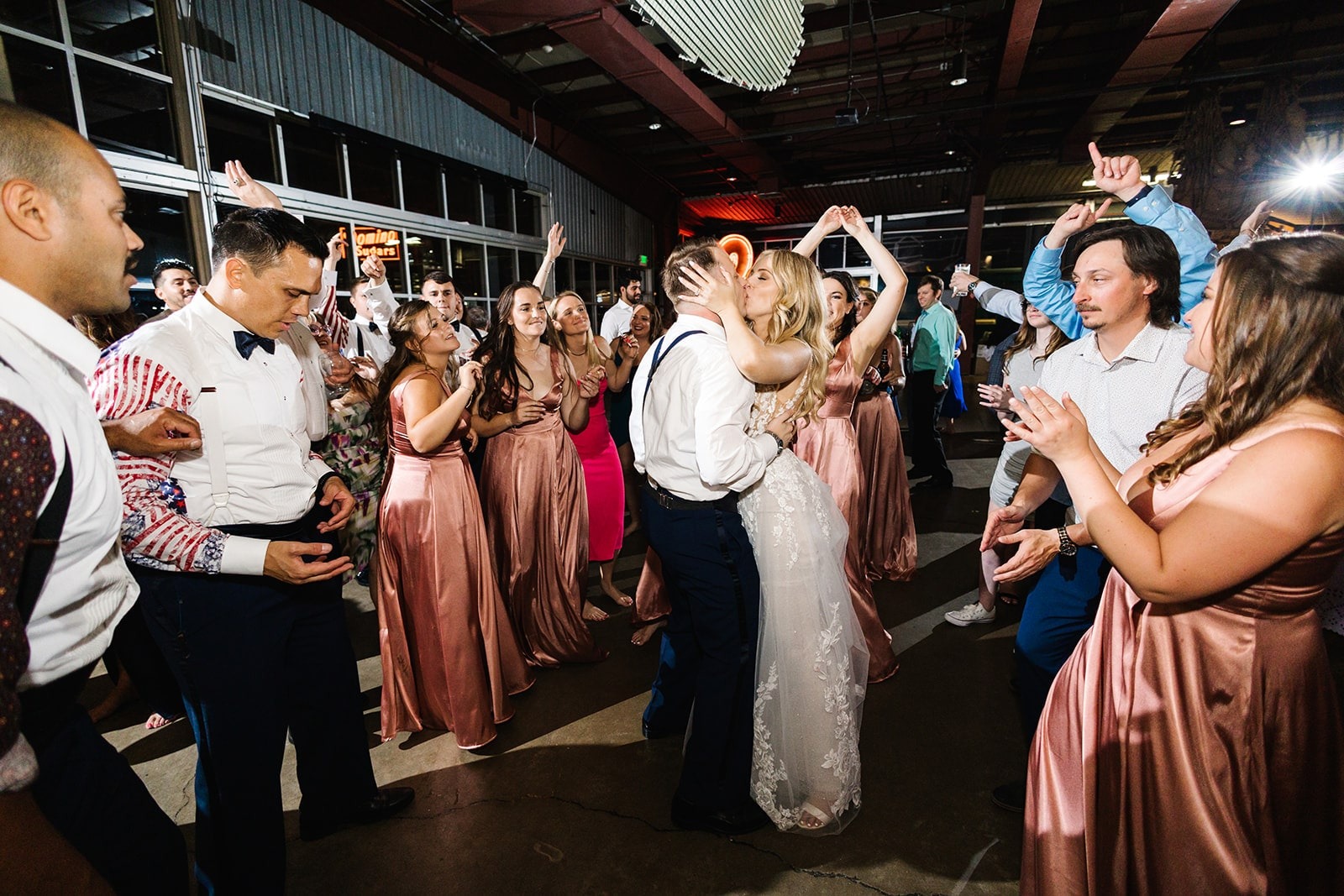 bride and groom kiss while guests dance around them