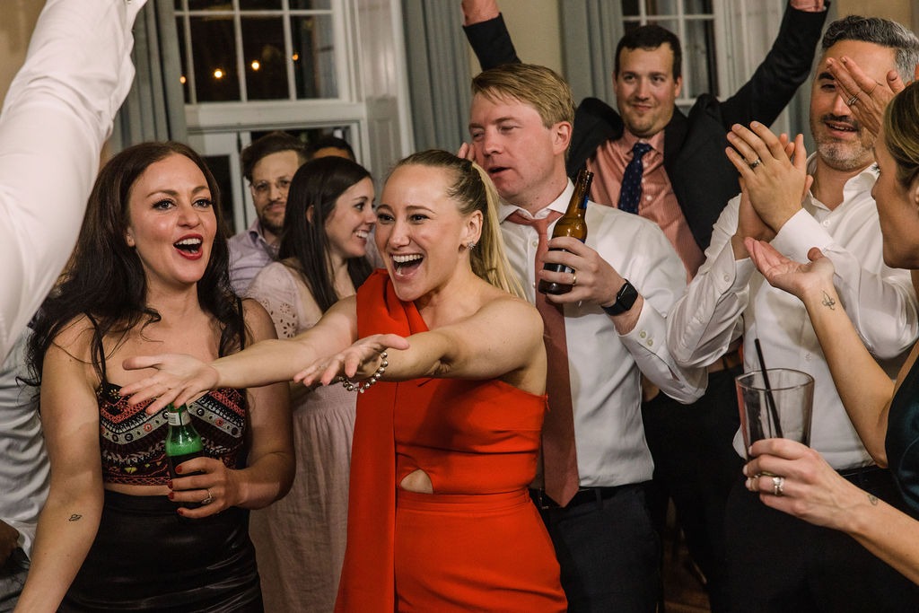 woman in red dress smiling and holding out hands while dancing surrounded by guests