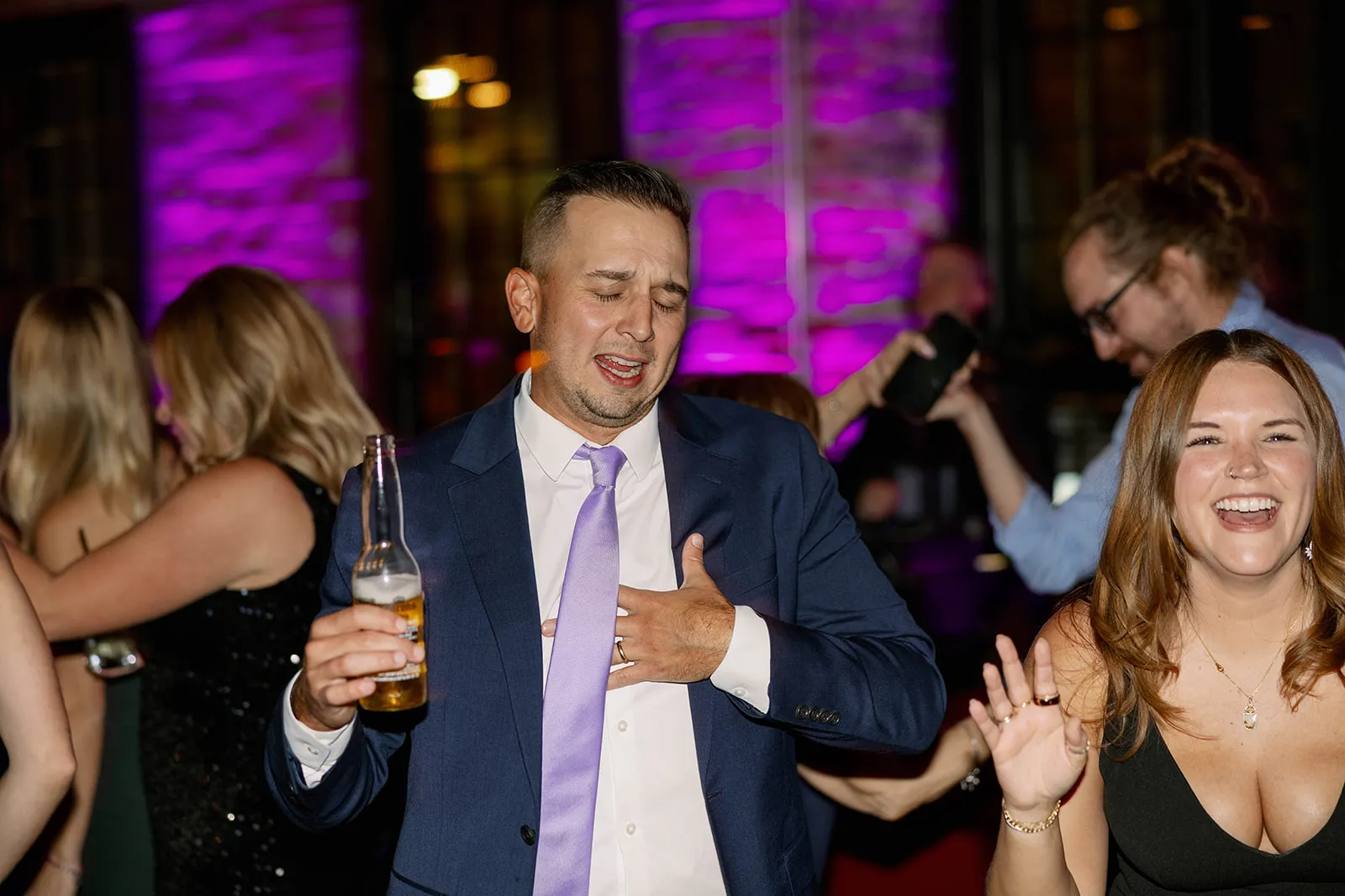 guy in navy suit and purple tie dancing at wedding with a beer in hand