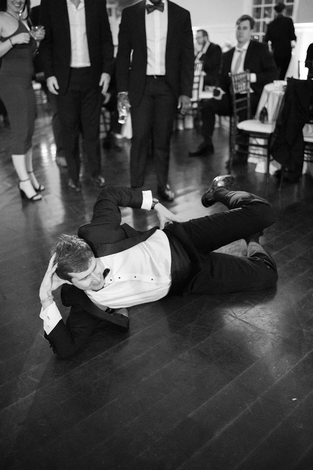 guy in tux posing laying down on floor at wedding dance floor