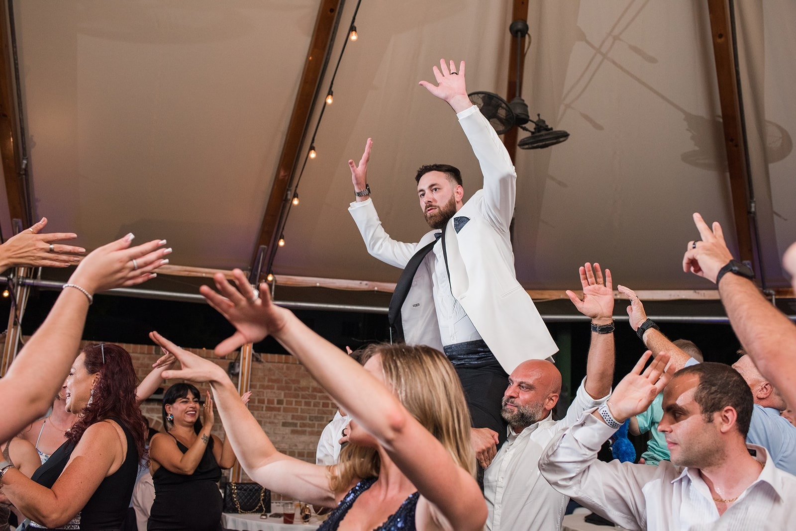 groom up on guys shoulders at wedding while guests dance