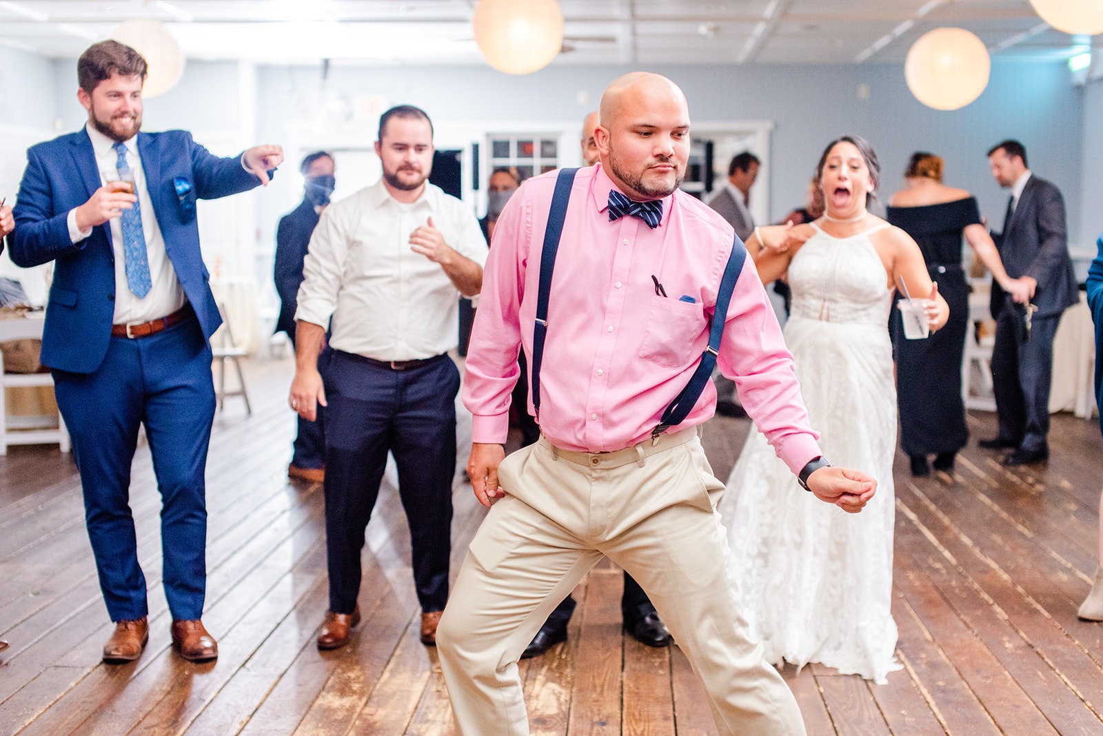 guy in pink shirt and bowtie dancing at wedding while guests and bride watch