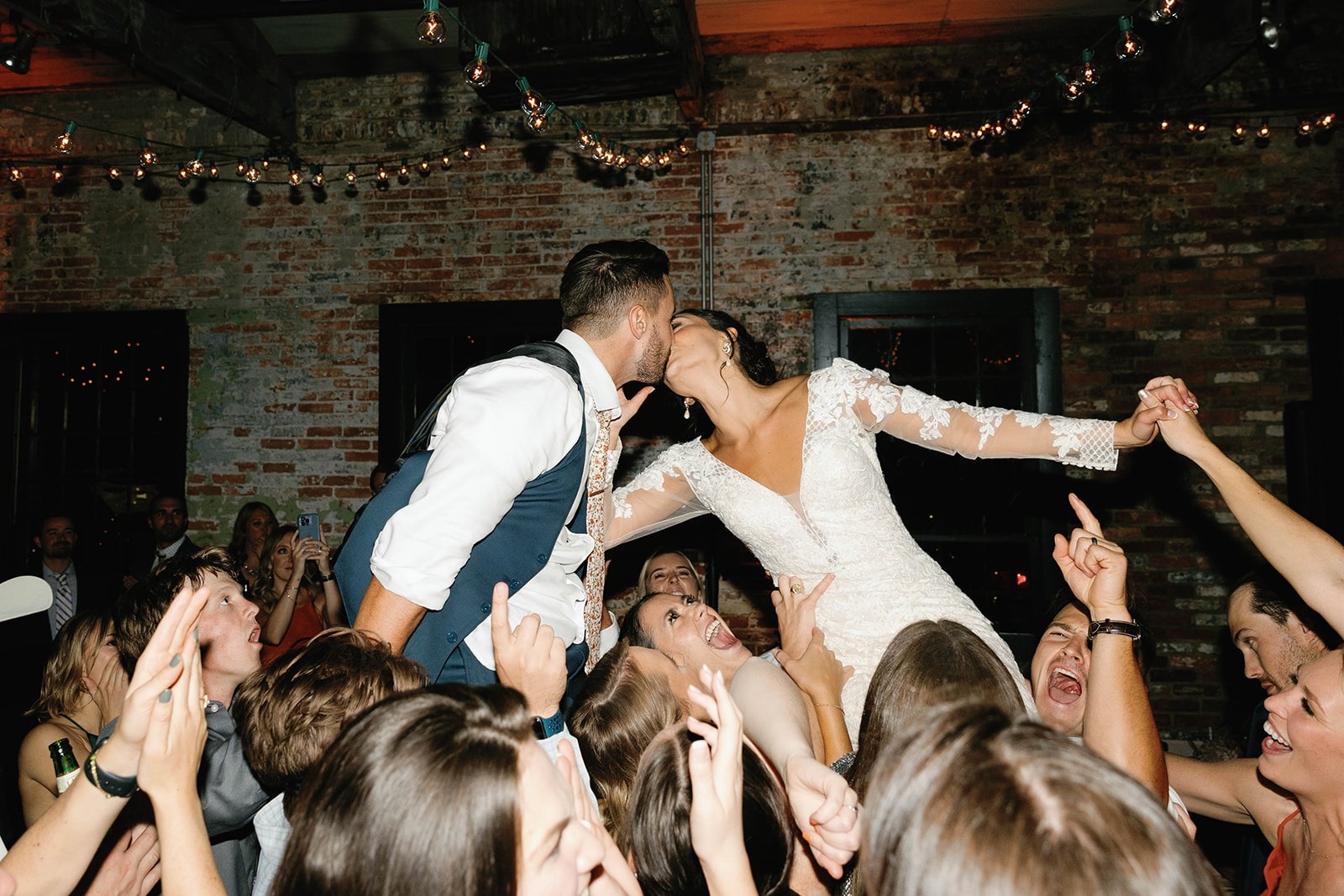 bride and groom kiss while up on shoulders of guests on dance floor