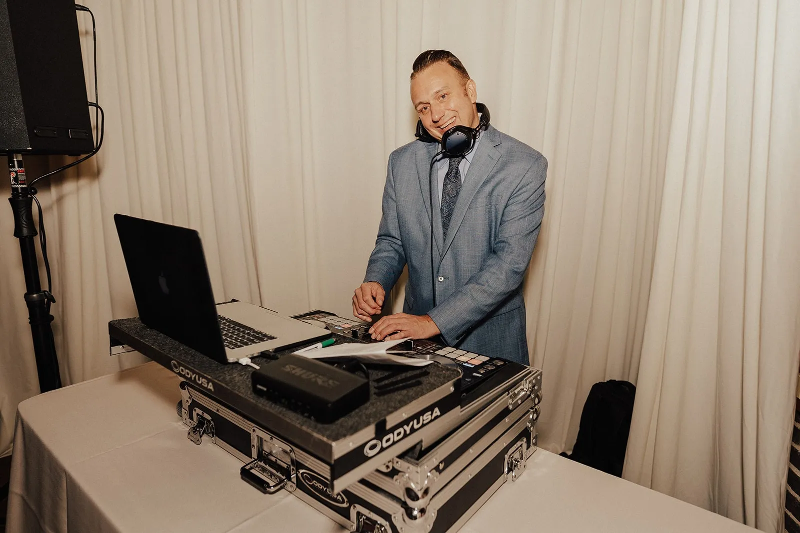 dj spinning music and smiling in front of white drape backdrop