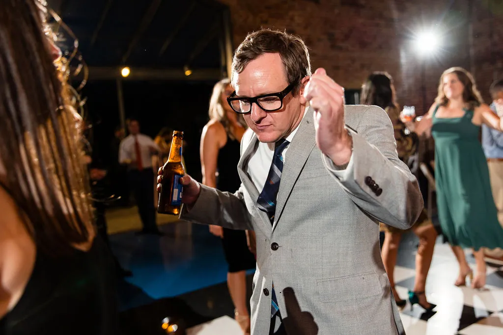 man with glasses in a grey suit dancing with beer bottle in hand