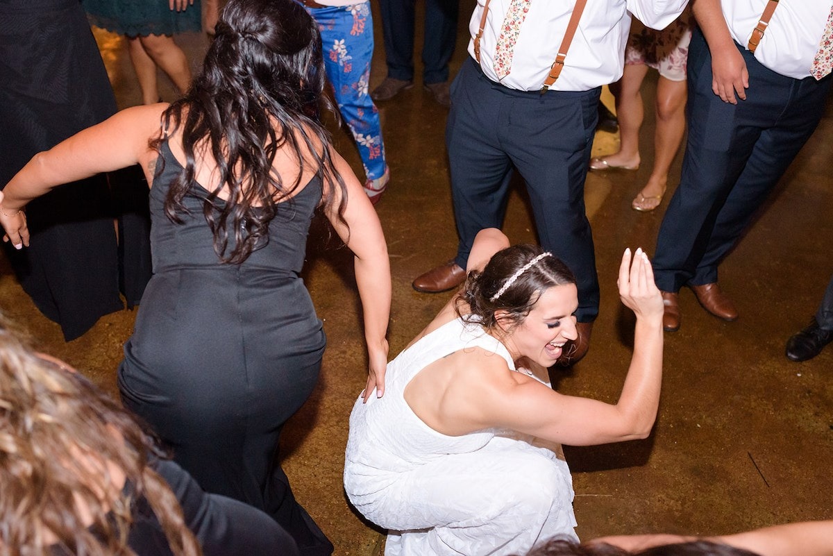 bridesmaid in black dress slapping bride on the butt while she dances squatting down to the floor