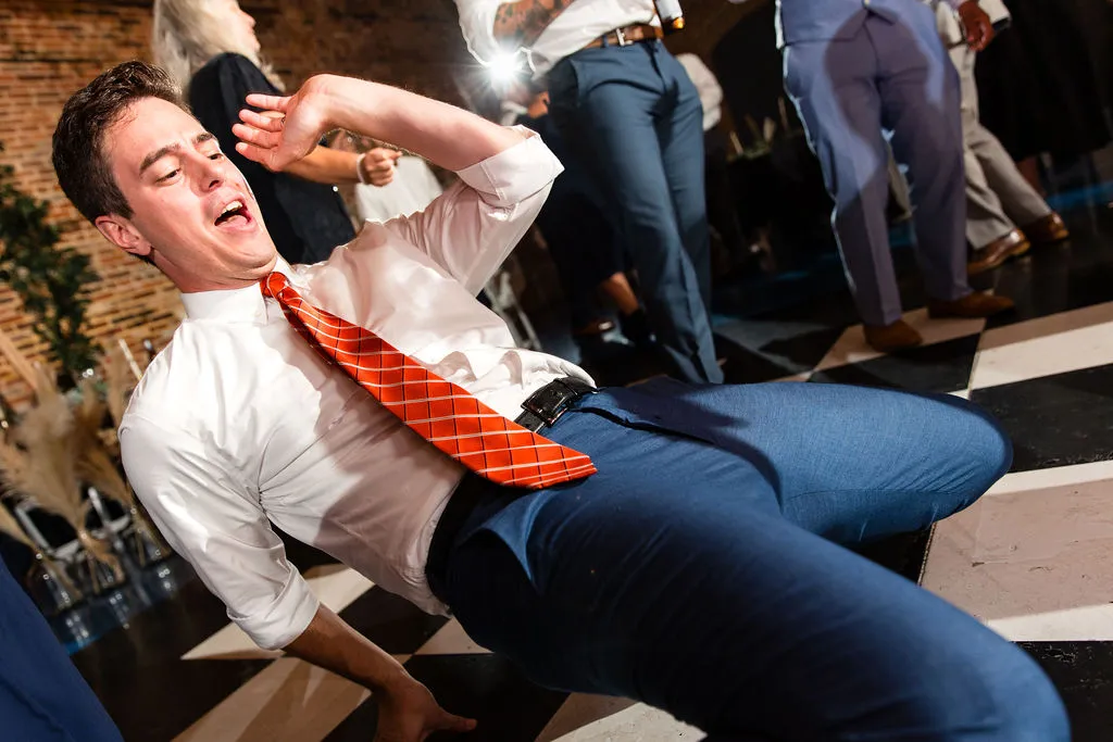 guy in white shirt, orange tie, and blue pants bent low on the dance floor