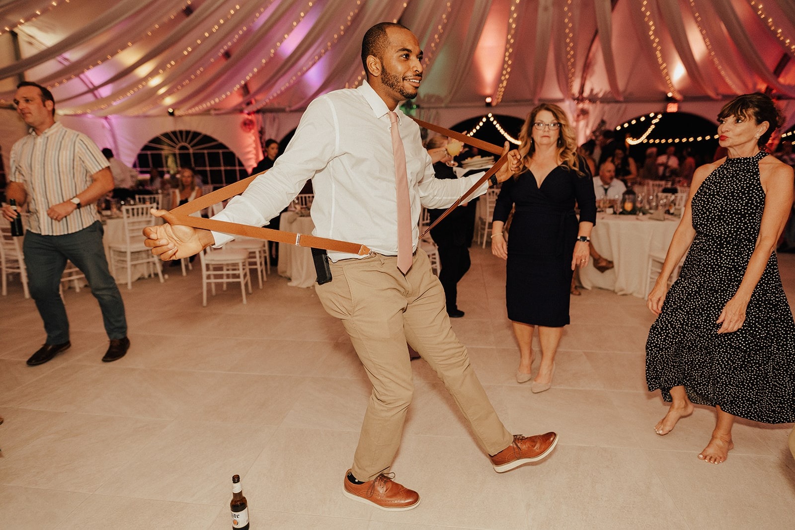 groomsmen dances around beer bottle and stretches suspenders