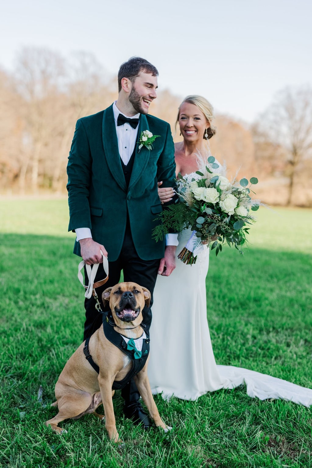 bride and groom pose with their dog on lawn during the day