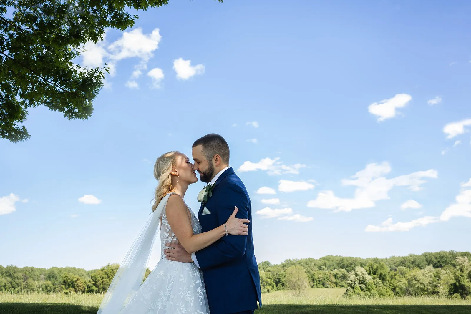 bride and groom kiss in front of a cloud-filled sky