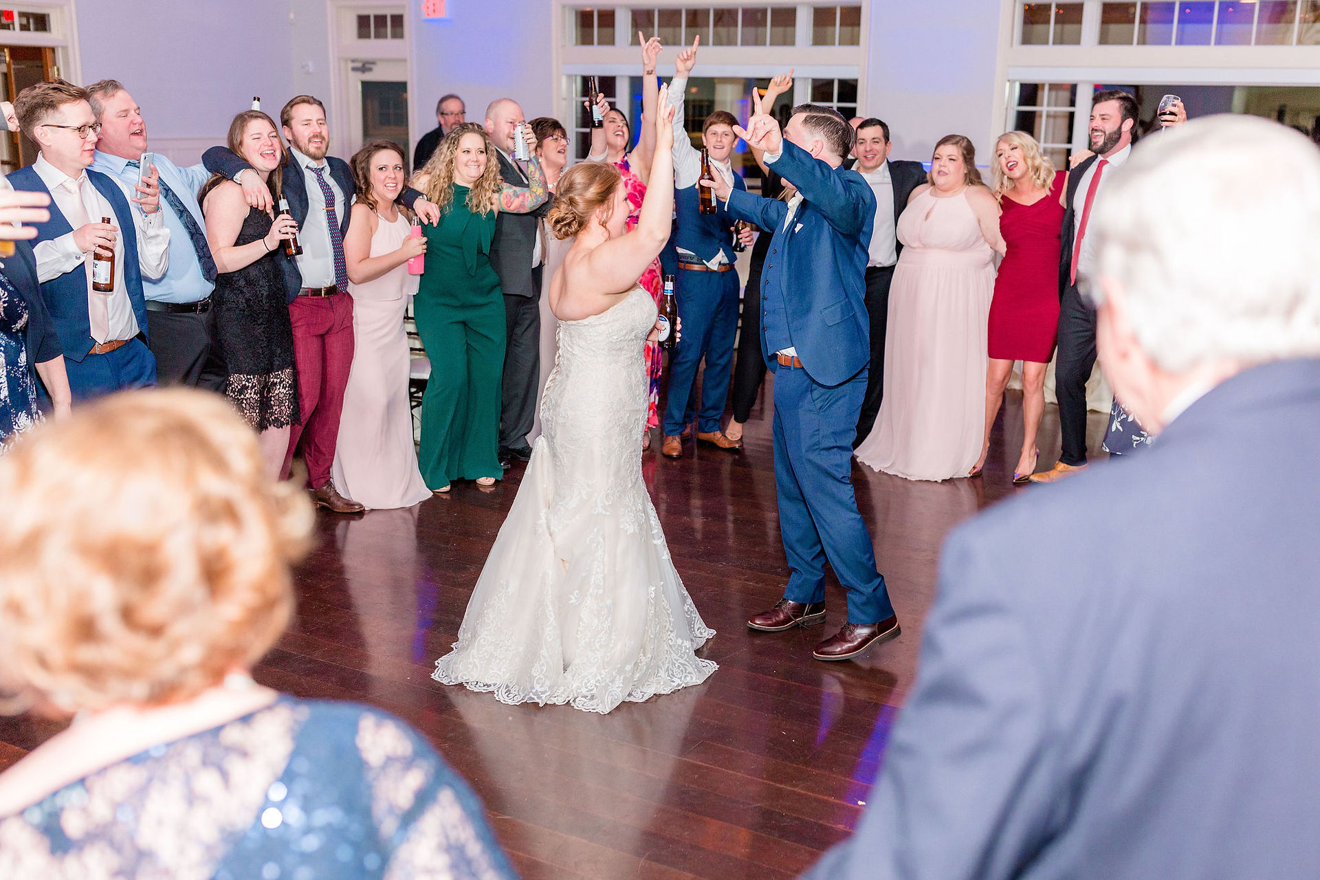 bride and groom dance with hands up and guests surround them