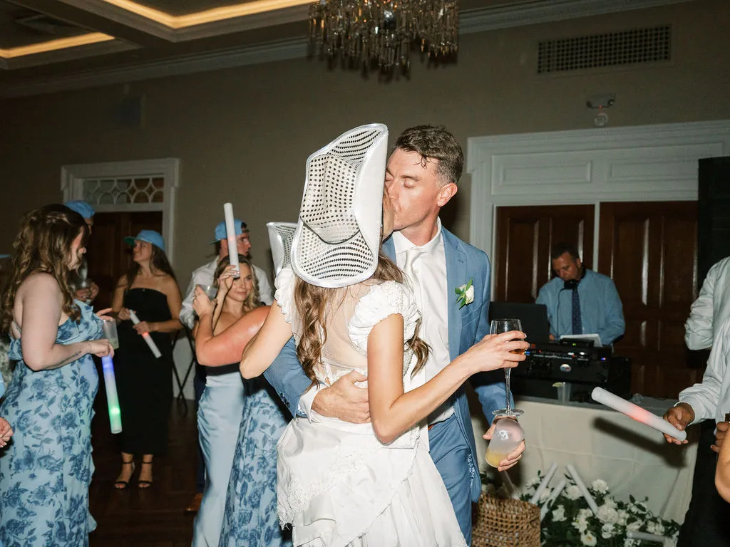 groom kissing bride while she is wearing a sparkly cowboy hat