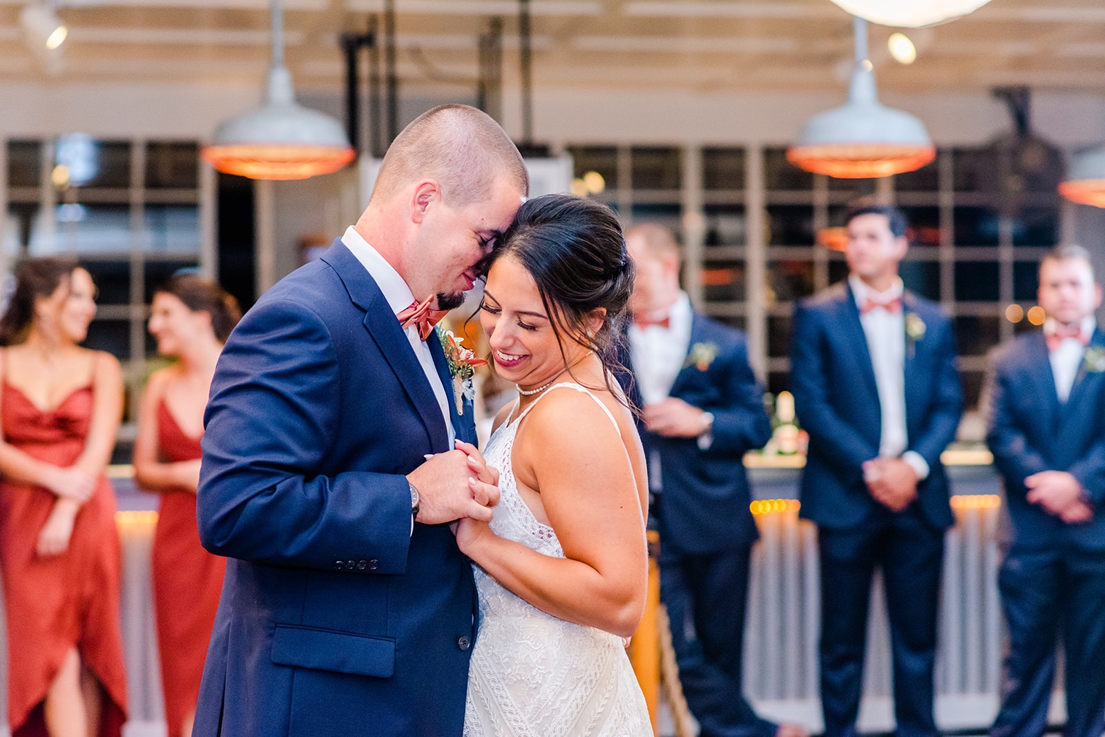 bride and groom first dance while wedding party watches in the background