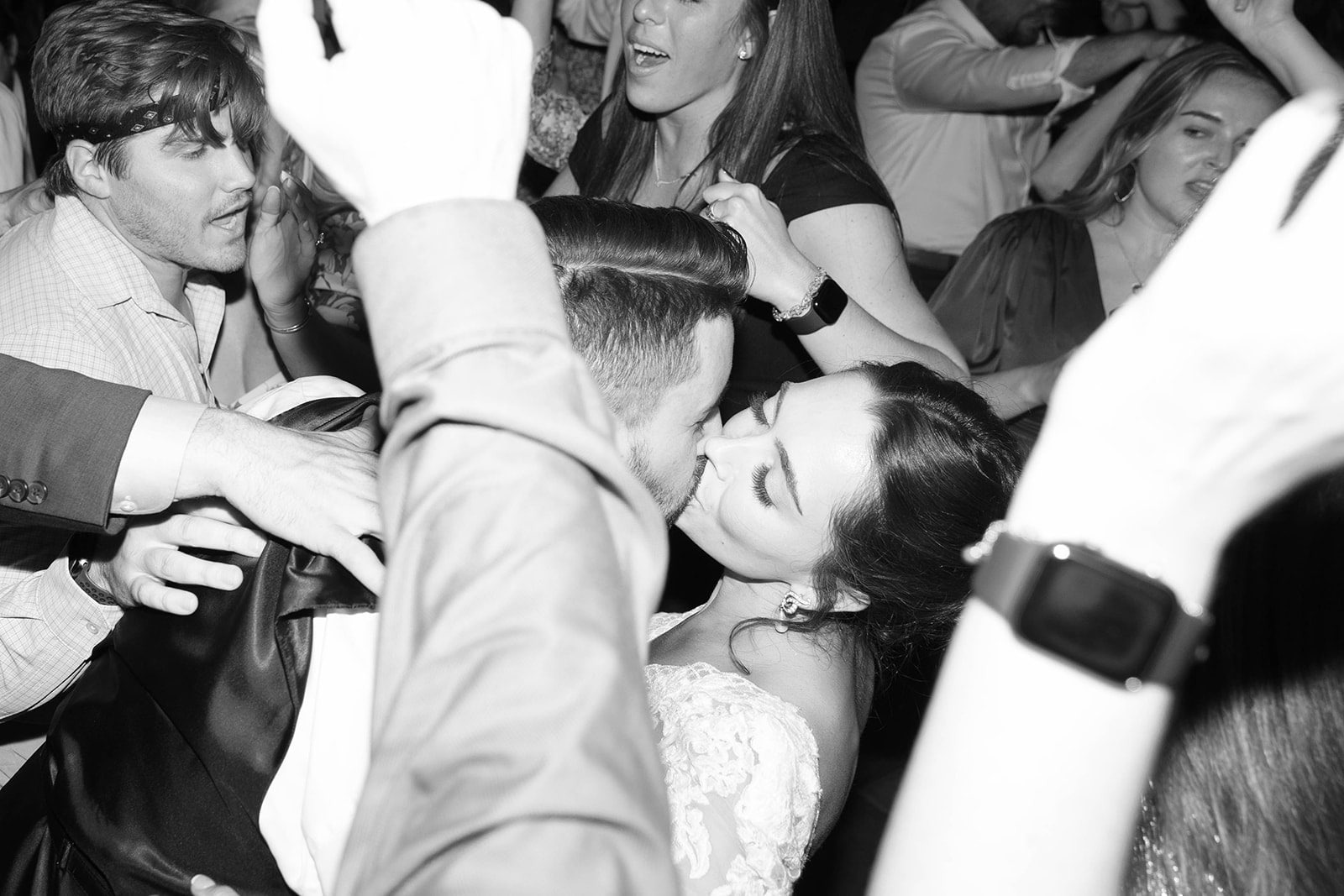 bride and groom kiss while surrounded by guests hands