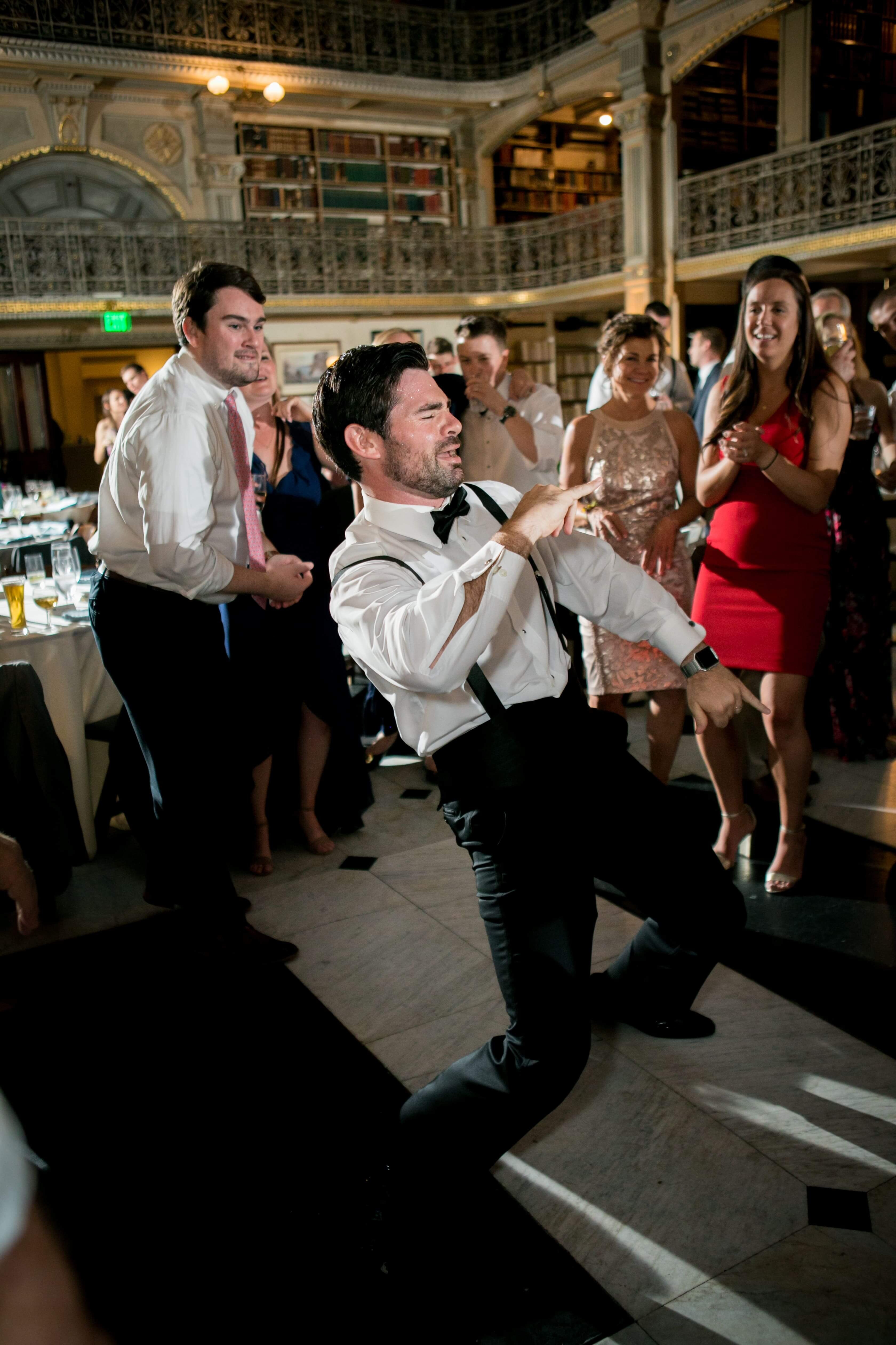 groomsman in bow tie and suspenders dancing at wedding