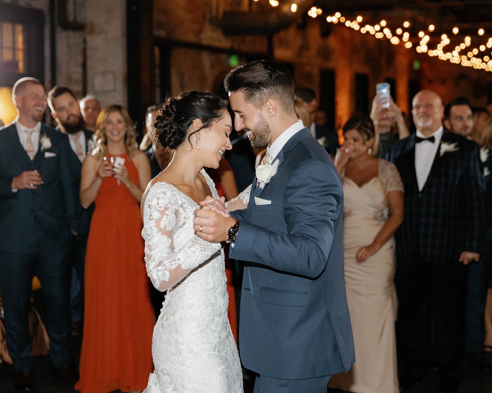 bride and groom first dance while guests watch in the background