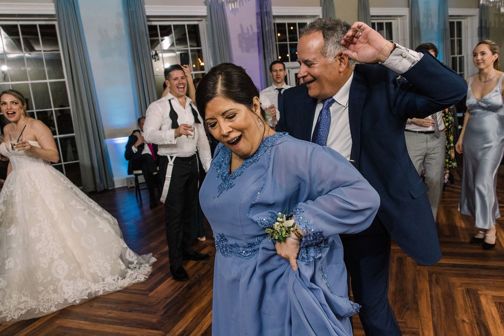 woman in blue dress dancing with man behind her while bride watches