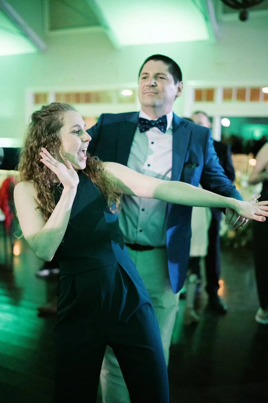 woman dancing with arms outstretched in front of man wearing a bow tie