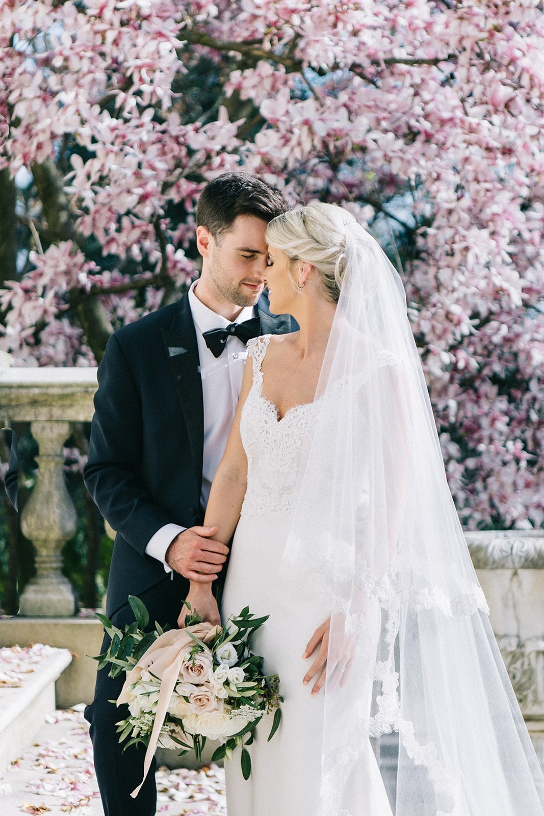 brie an groom pose in front of tree blossoms