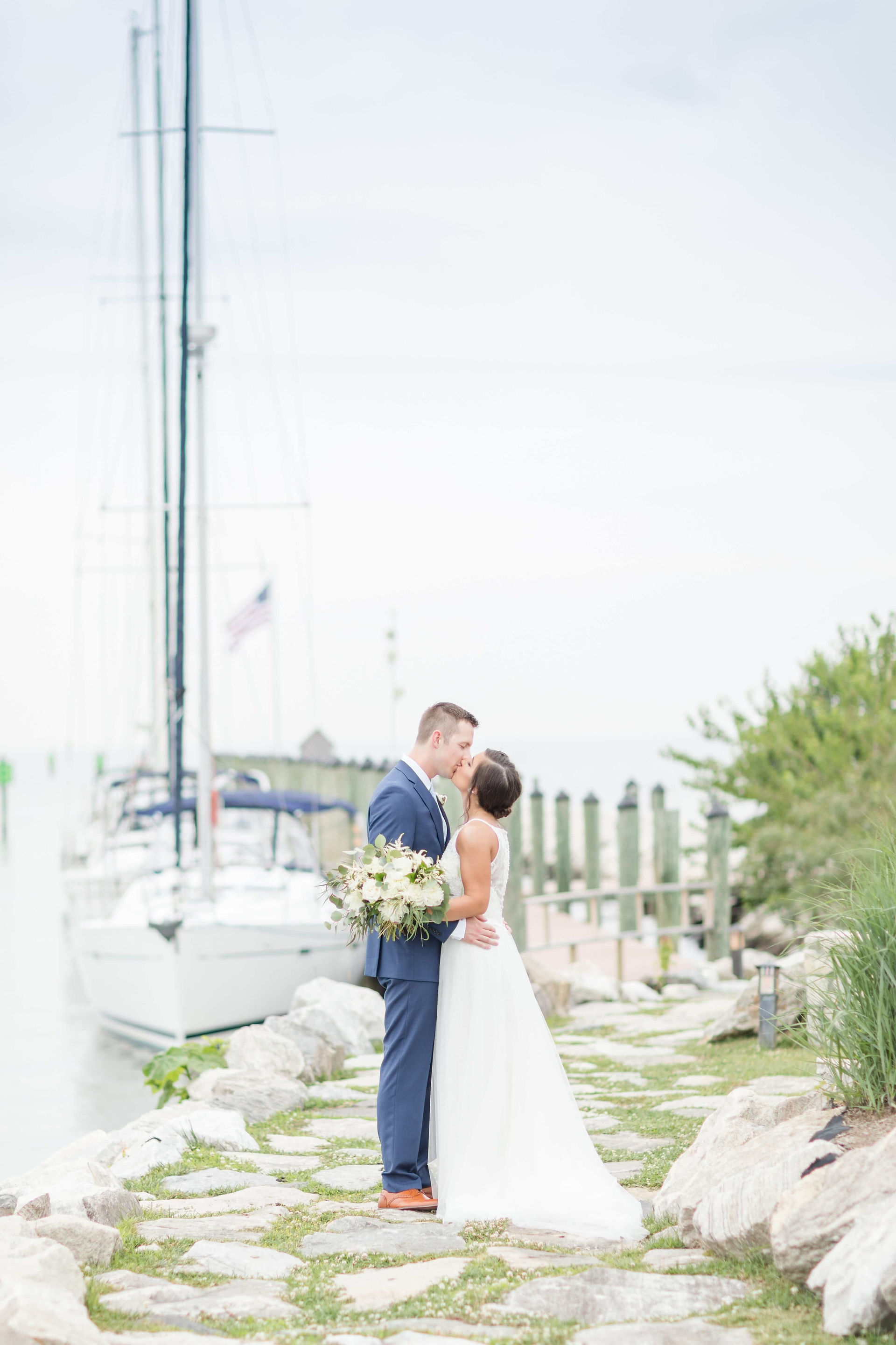 bride and groom kiss in front of sailboat
