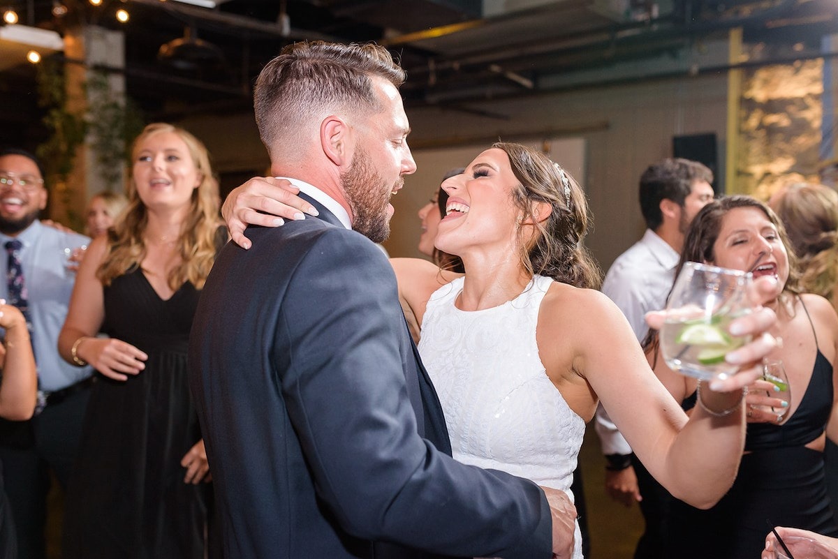 bride with drink in hand and groom dancing together 