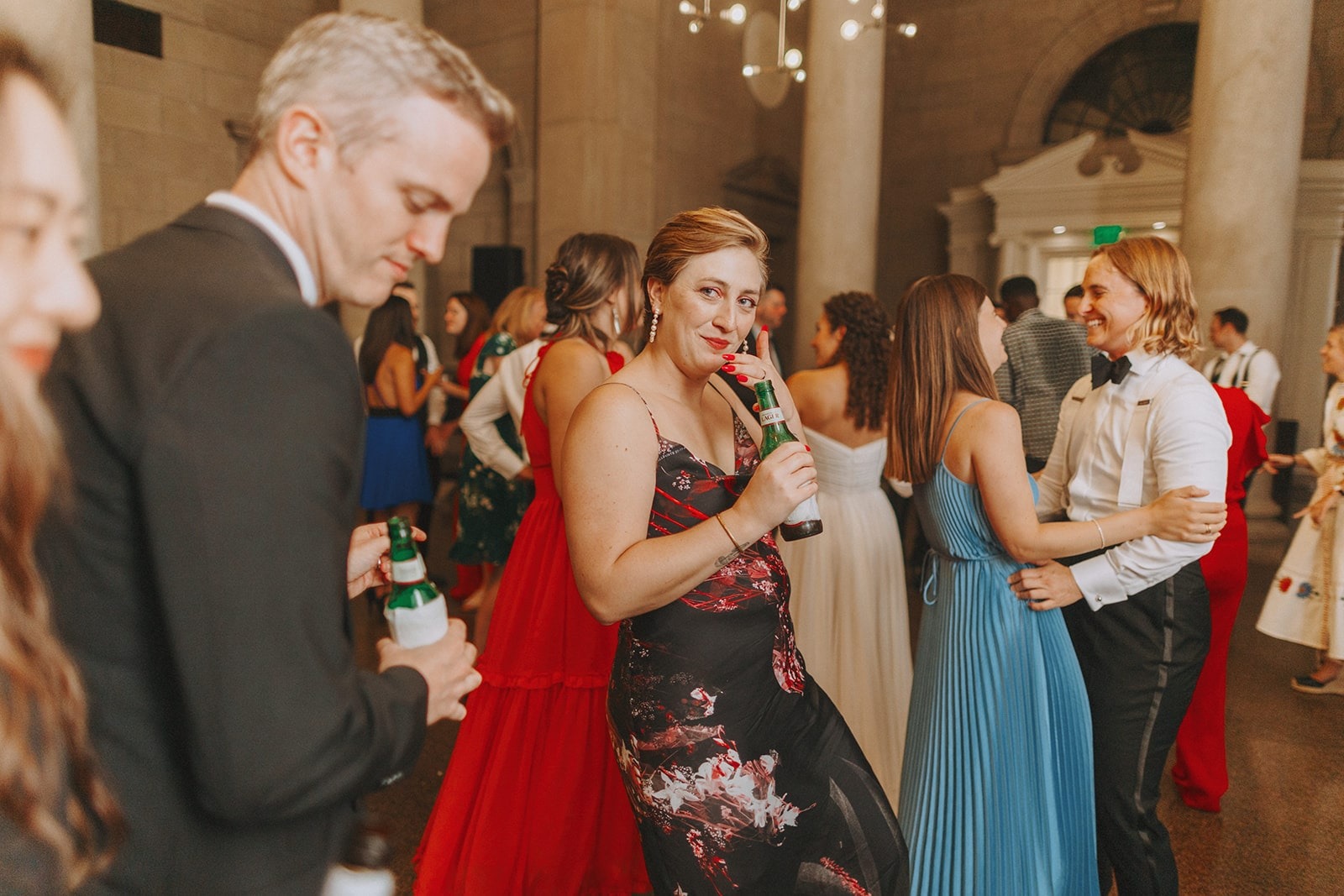 woman in black and pink dress dancing with beer in hand at wedding