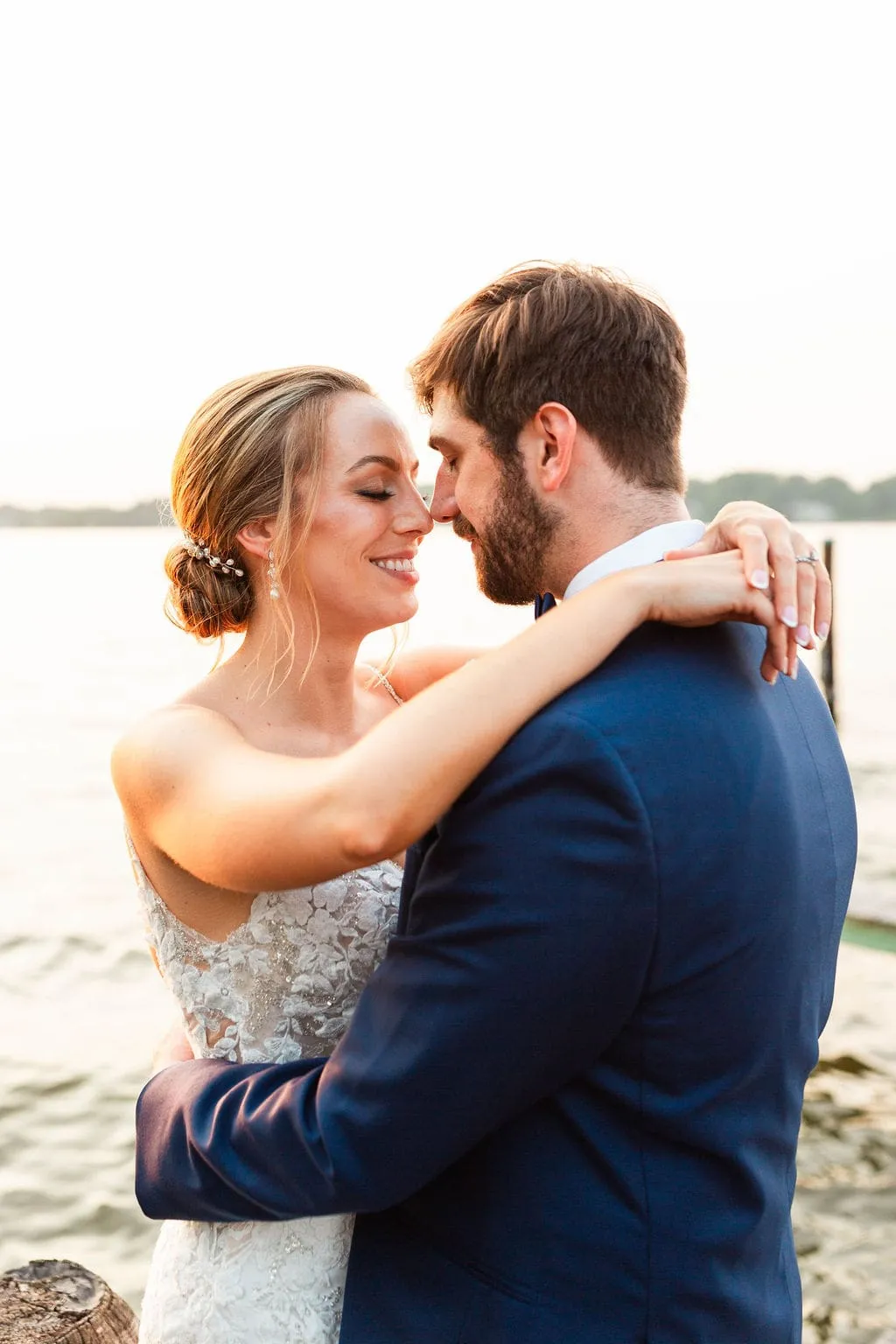bride and groom pose by water during sunset