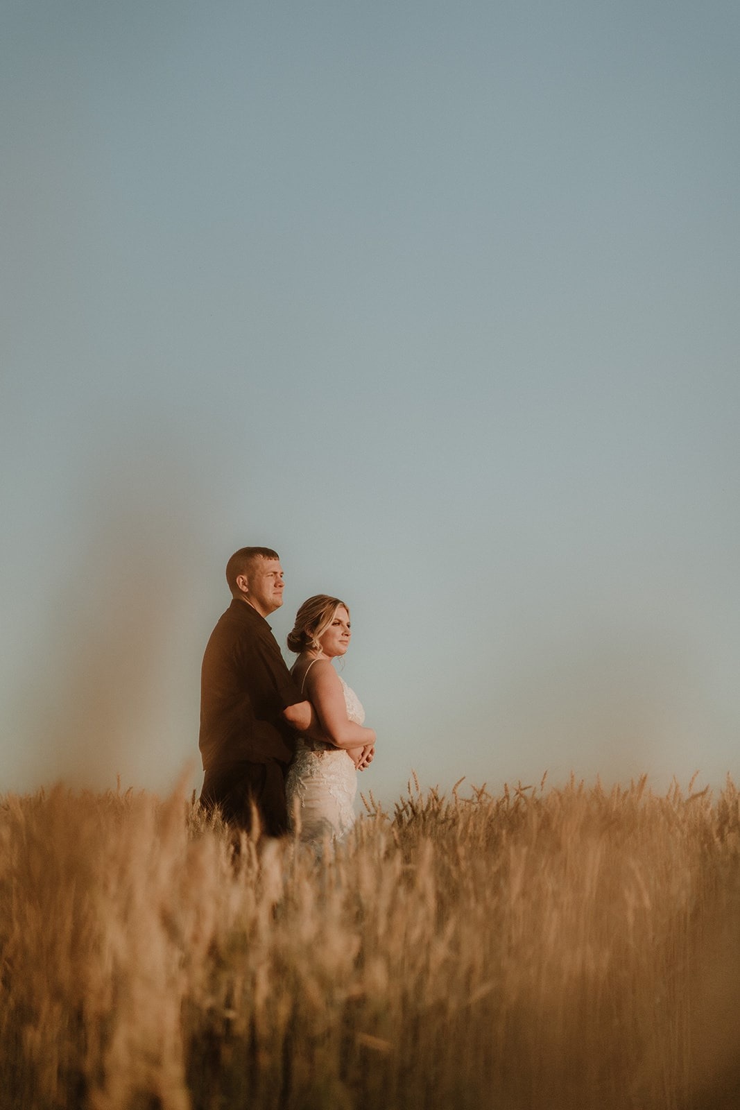 bride and groom posing together in wheat field during sunset