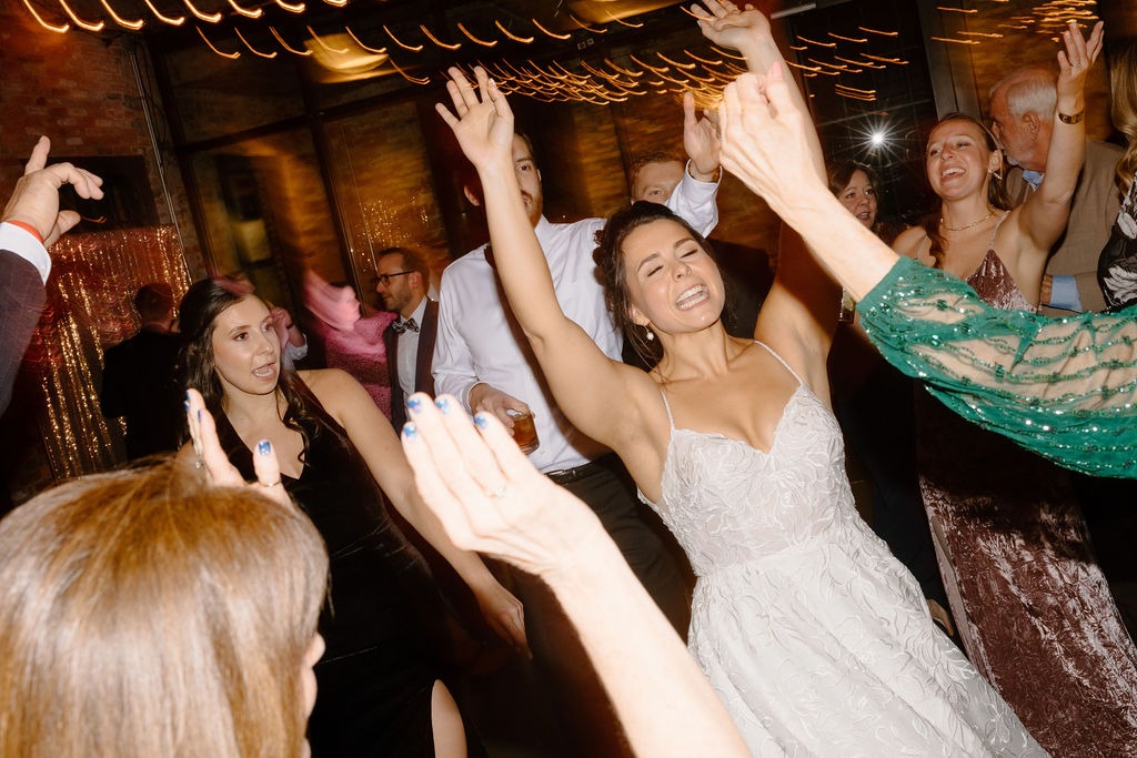 bride dancing with friends while raising up arms