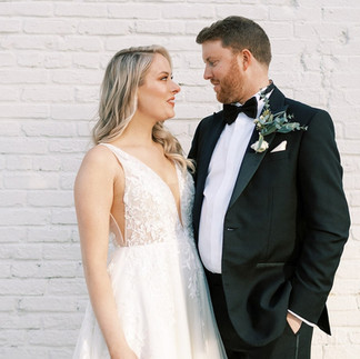 bride and groom pose in front of white brick wall