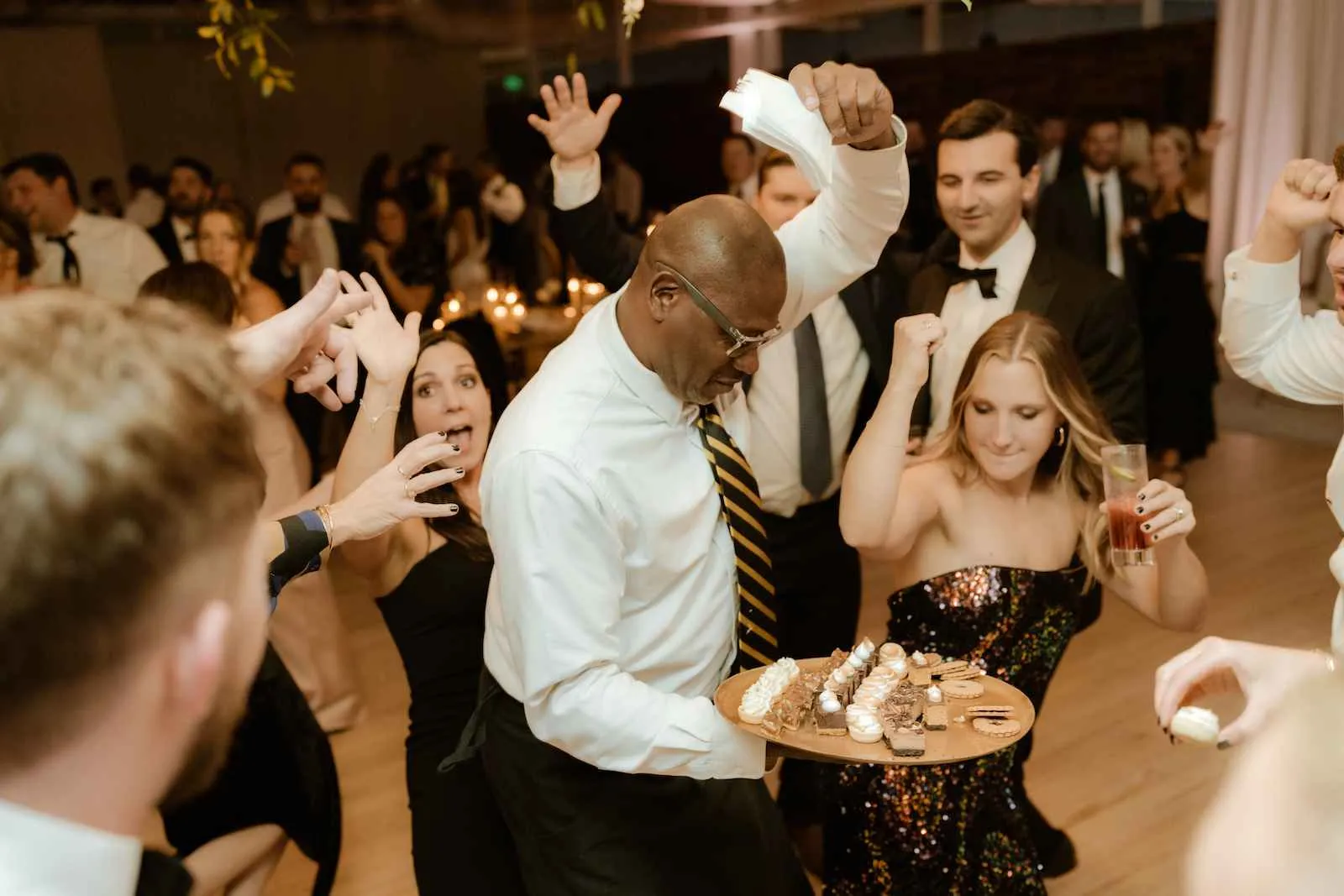 server holding a plate of late night treats dancing at the center of the floor surrounded by guests