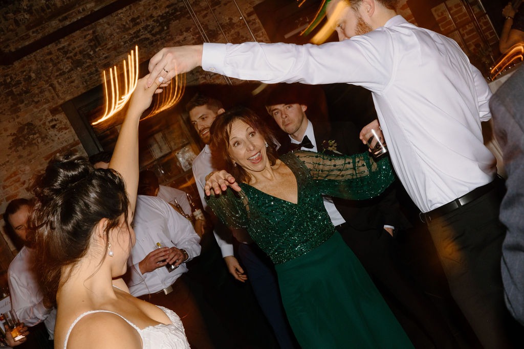 mother in green dress dancing underneath raised and connected arms of bride and groom