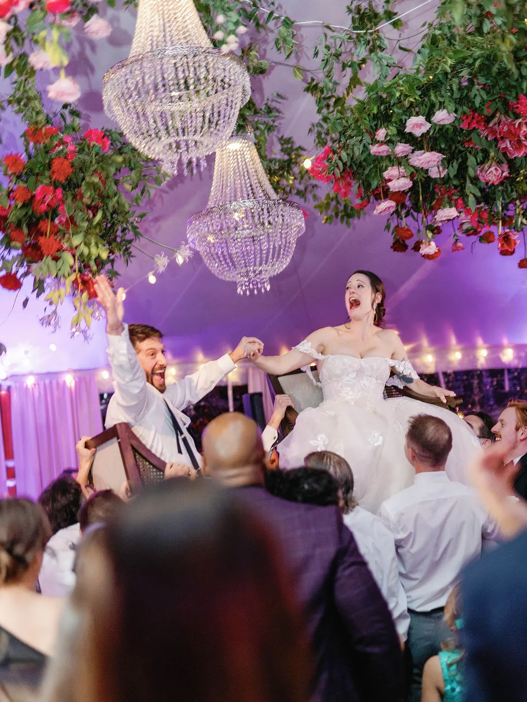 bride and groom lifted up in chairs underneath chandliers