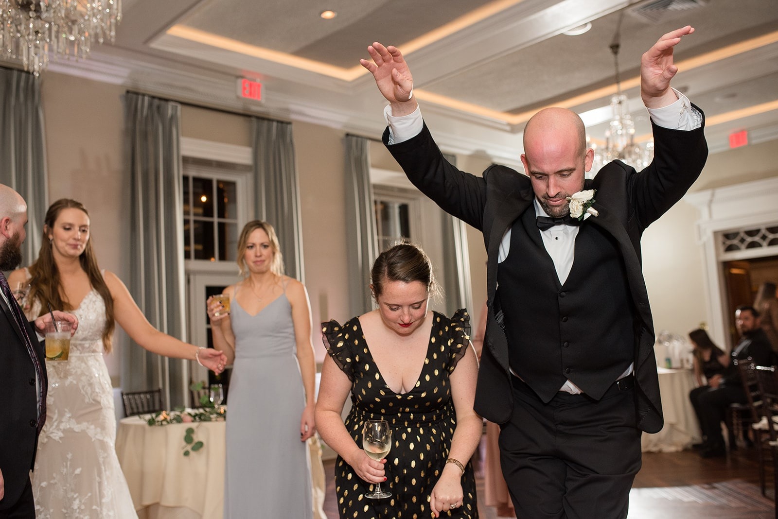 groom dancing with hands up while next to woman holding a glass of wine