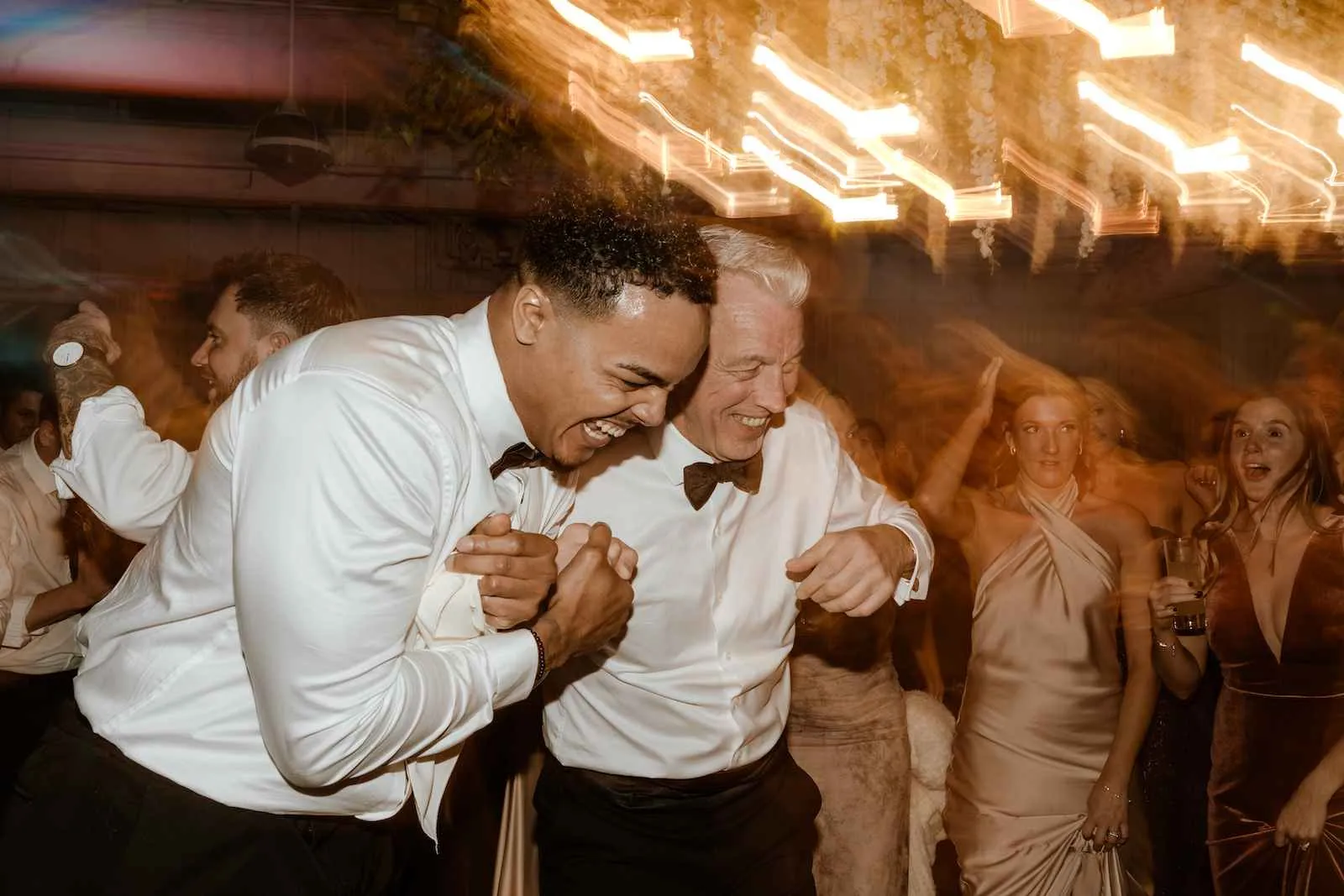 young groomsman and older man holding hands and laughing while dancing at wedding