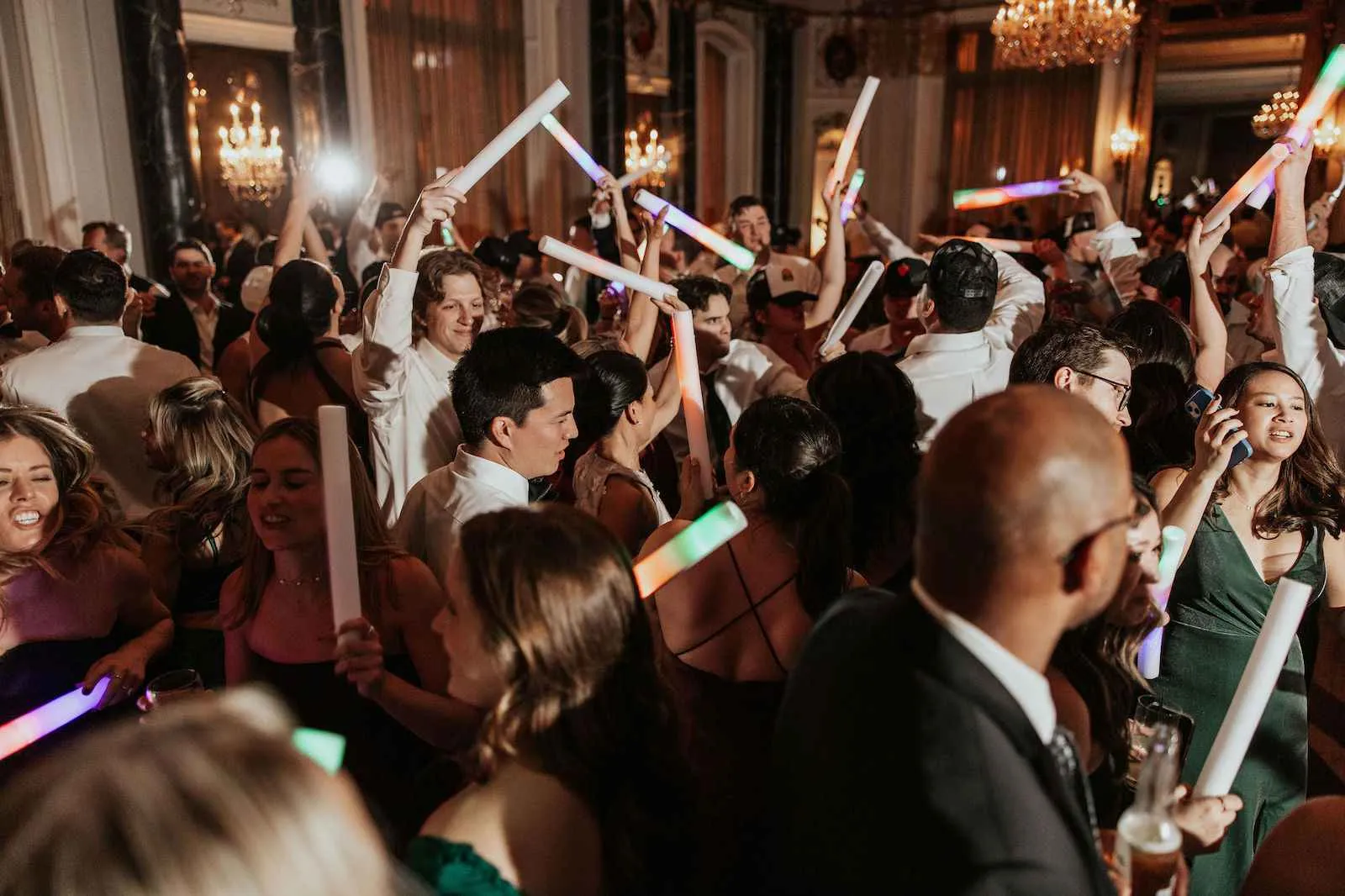 wedding guests dancing with light sticks in ballroom