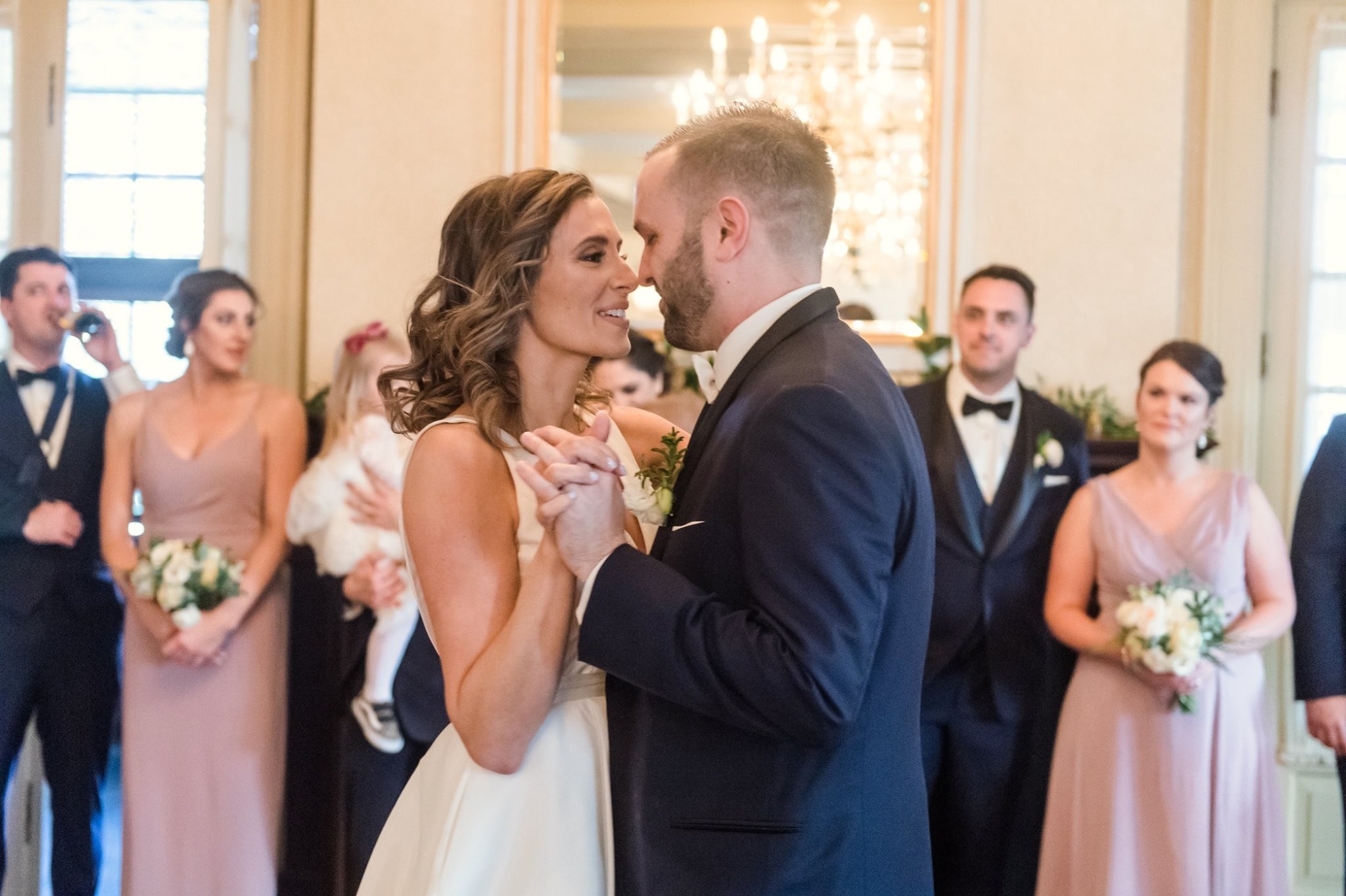 bride and groom first dance while wedding party watches