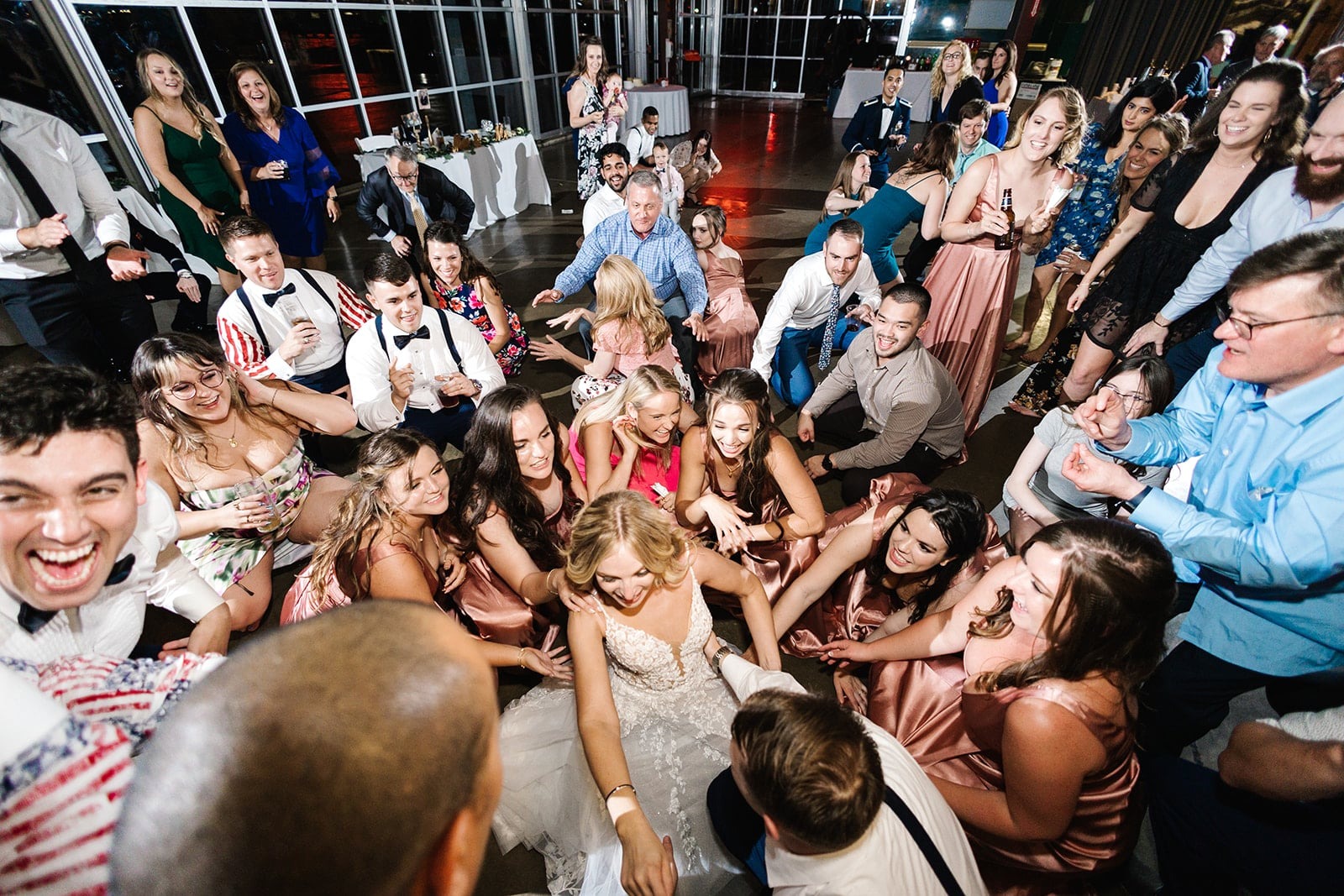 bride surrounded by guests as they squat down on dance floor