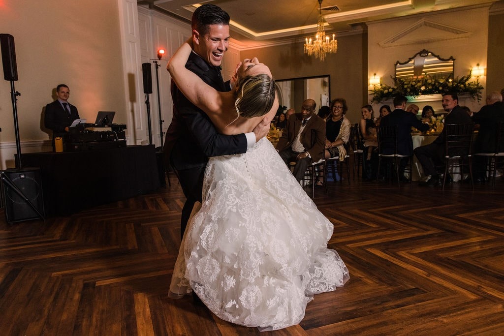 groom dipping bride during first dance while guests watch from tables