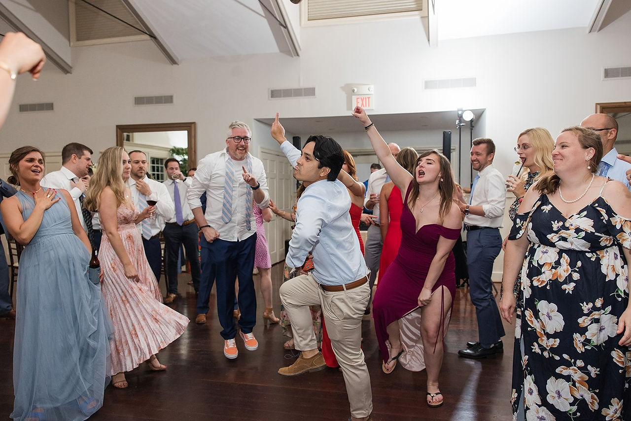 guy in kahki pants with hand up dancing in middle of group at wedding