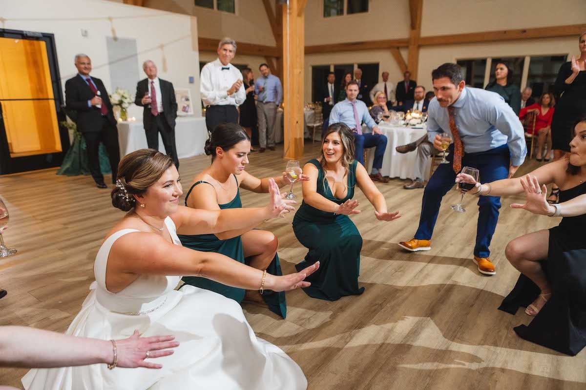 bride and women in green dresses squatting down on the dance floor with hands outstretched