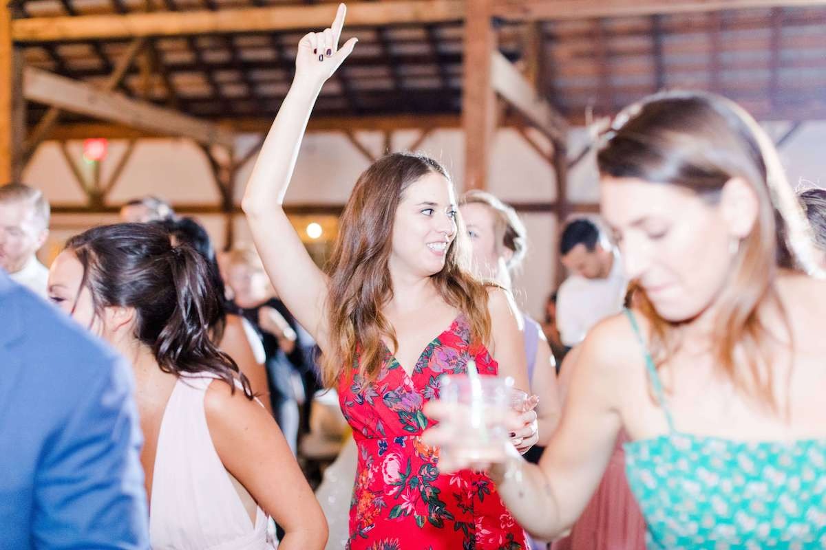 brunette in red flower dress dancing with hand up at wedding