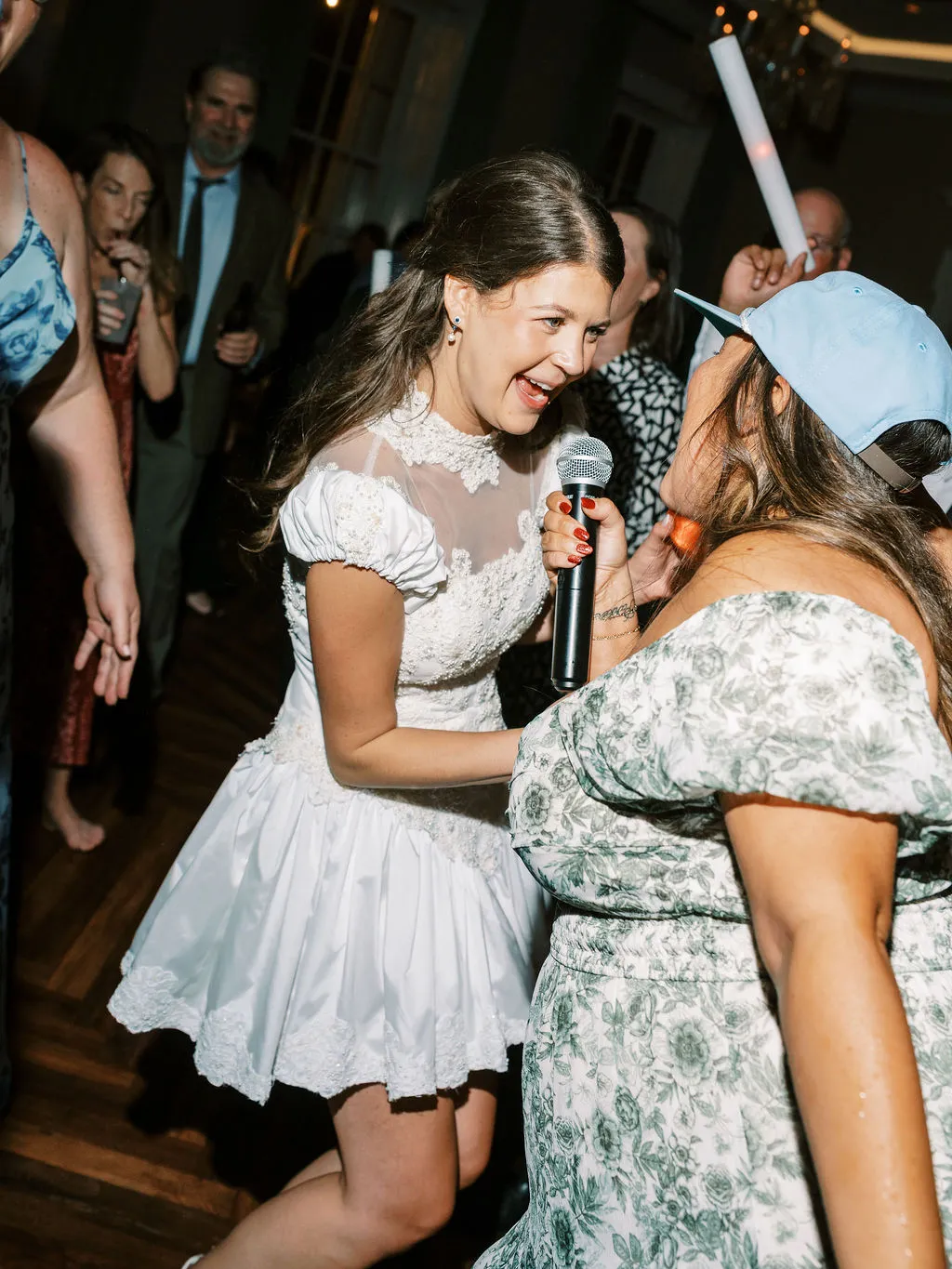 bride wearing short, white dress dancing with woman in blue baseball cap