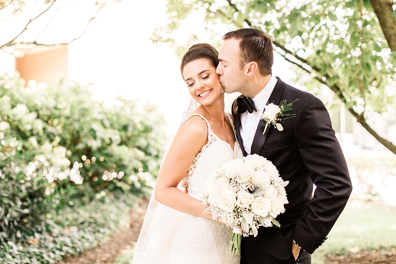 groom kisses brides cheek out in garden