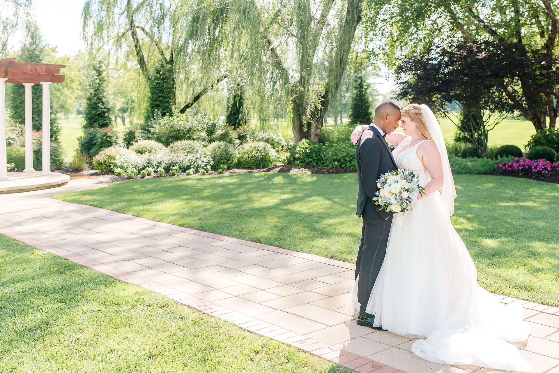 bride and groom pose on path by garden